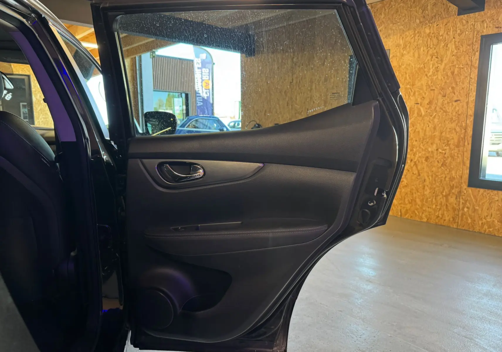 Vue intérieure de la porte arrière gauche noire du Nissan Qashqai II PH2, avec garniture en cuir et poignée chromée.