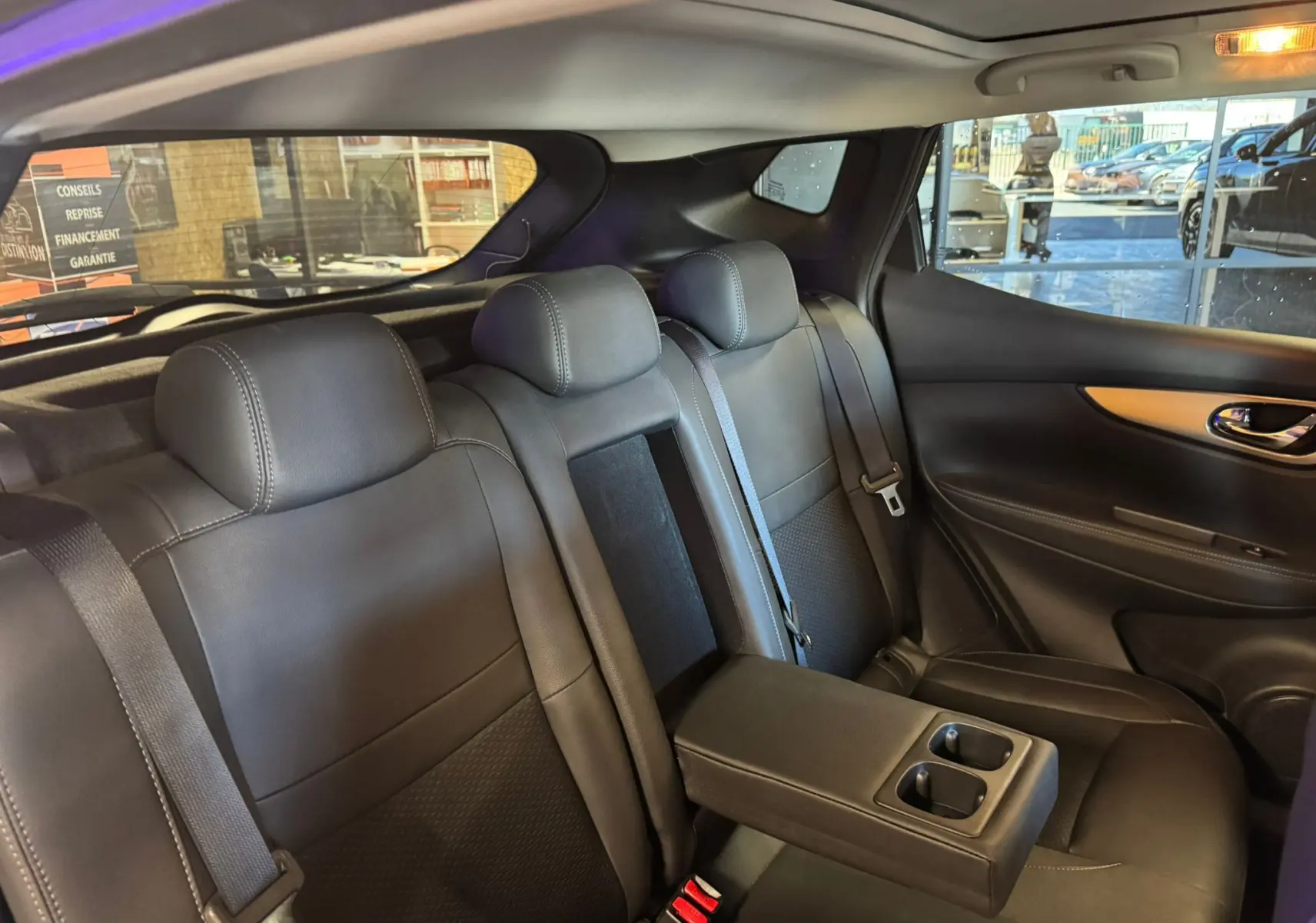 Vue intérieure arrière du Nissan Qashqai noir avec banquette cuir, accoudoir central et ceintures visibles.