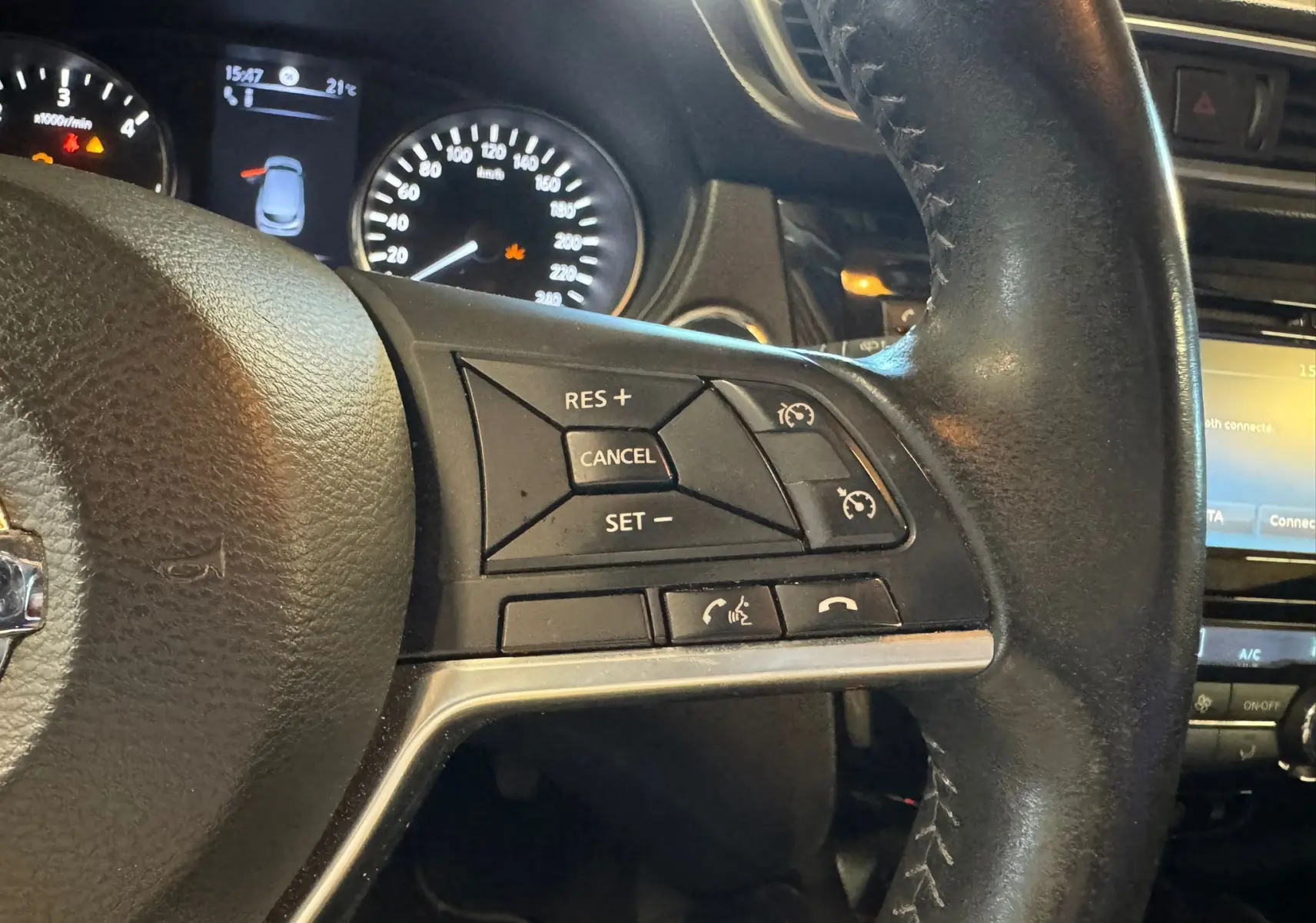 Gros plan sur le volant cuir multifonctions noir du Nissan Qashqai II PH2 avec commandes de régulateur de vitesse.