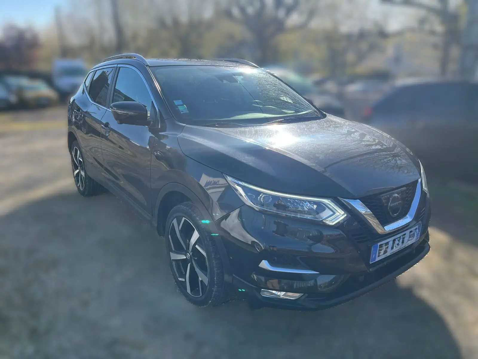 Vue de profil côté gauche d'un Nissan Qashqai noir 2017 avec jantes alliage et barres de toit en intérieur d'atelier.