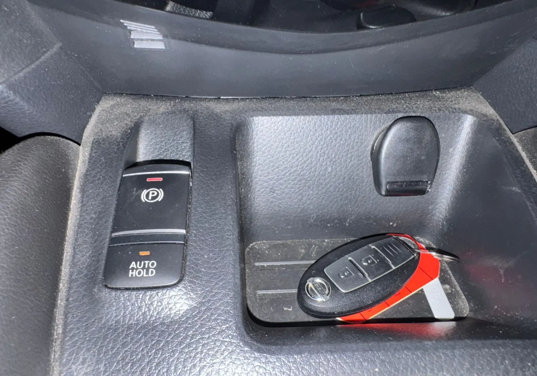 Gros plan sur la console centrale noire du Nissan Qashqai II avec clé main libre et bouton frein à main électrique.