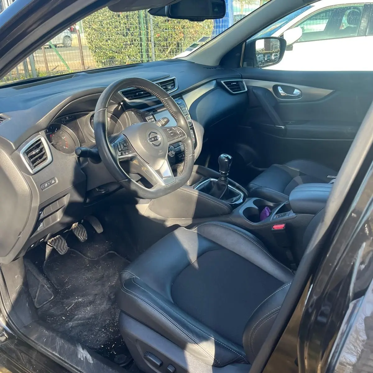 Vue 3/4 arrière droite du Nissan Qashqai noir avec jantes alu et barres de toit, stationné en intérieur lumineux.