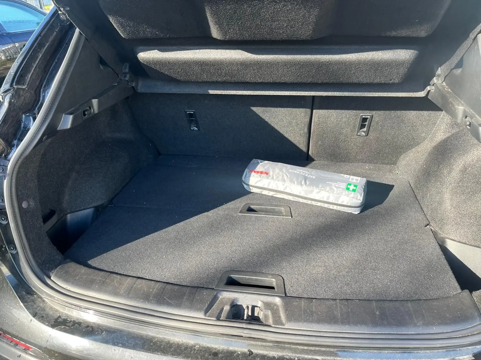 Vue 3/4 arrière droite d'un Nissan Qashqai noir 2017 avec jantes alu et barres de toit, stationné en intérieur.