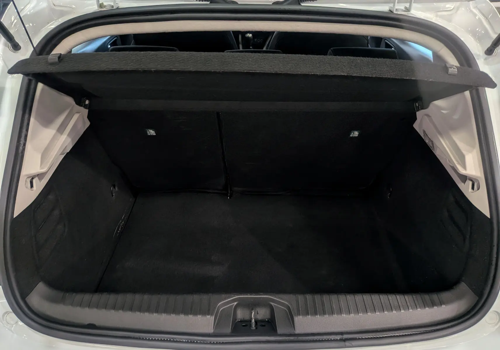 Coffre ouvert vu de l'arrière d'une Renault Clio V Blanc Glacier, montrant l'espace de chargement vide et la tablette arrière relevée.