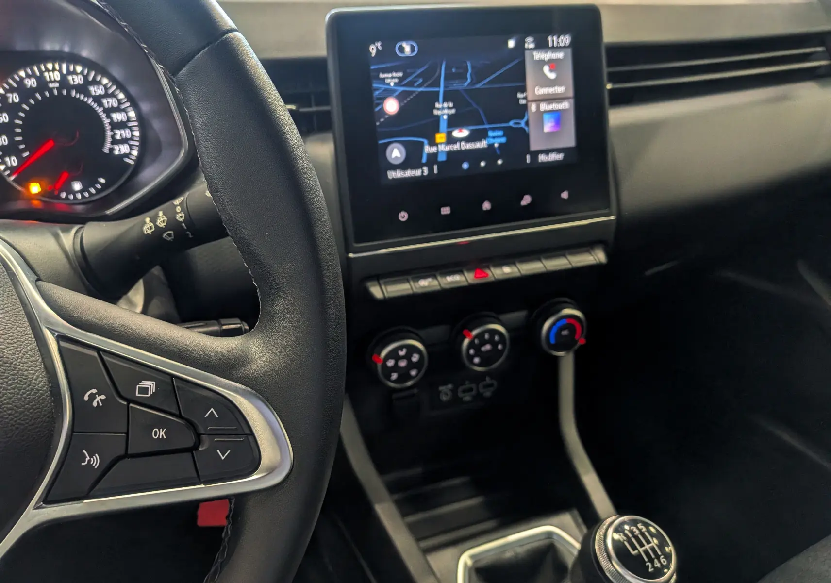 Vue intérieure centrée sur la console centrale et volant de la Renault Clio V Business 2020 avec écran tactile et levier de vitesse manuel.