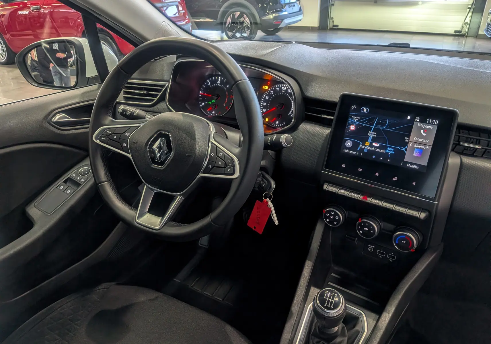 Vue intérieure côté conducteur de la Renault Clio V Business 2020, tableau de bord noir avec écran tactile et levier de vitesse manuel.