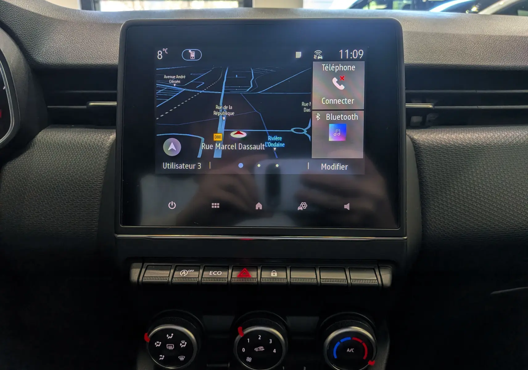 Vue rapprochée de l'écran tactile central et des commandes de climatisation d'une Renault Clio V blanche.