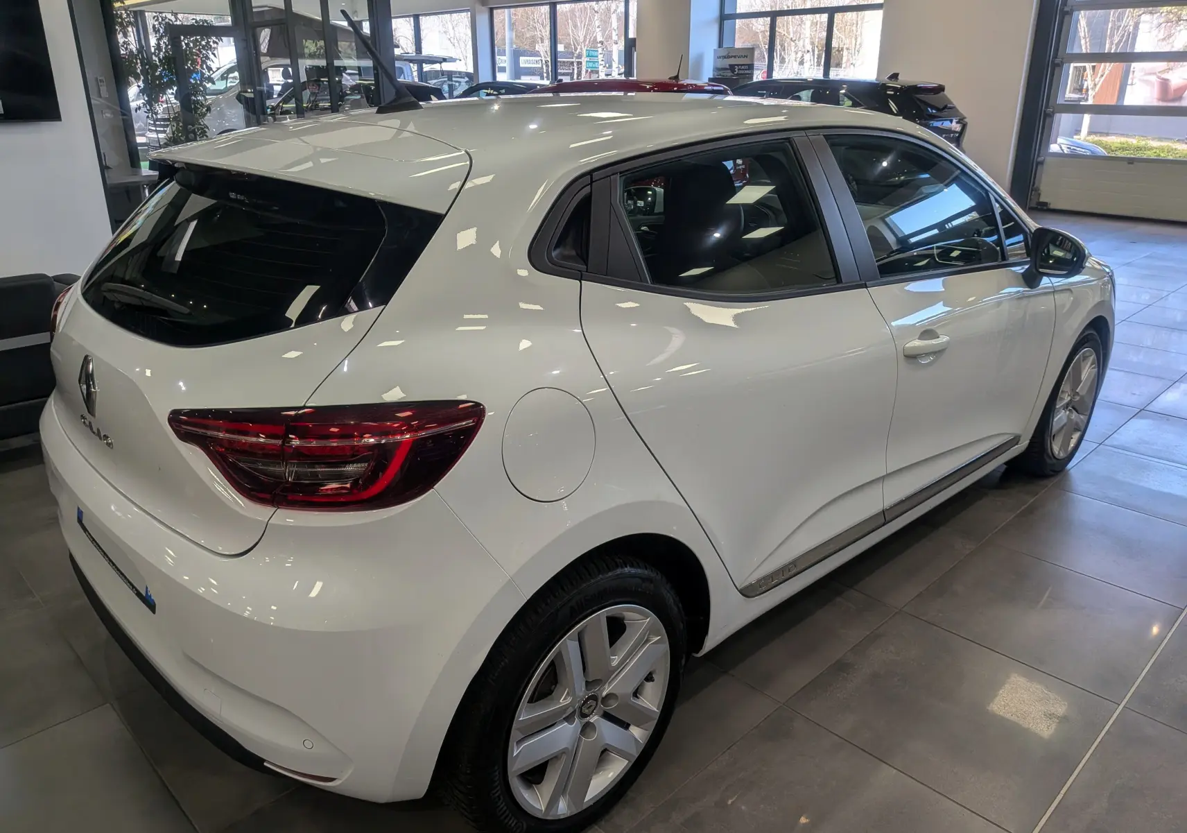 Vue 3/4 arrière droite d'une Renault Clio V Business blanc glacier en showroom, soulignant ses feux arrière LED et jantes alliage.