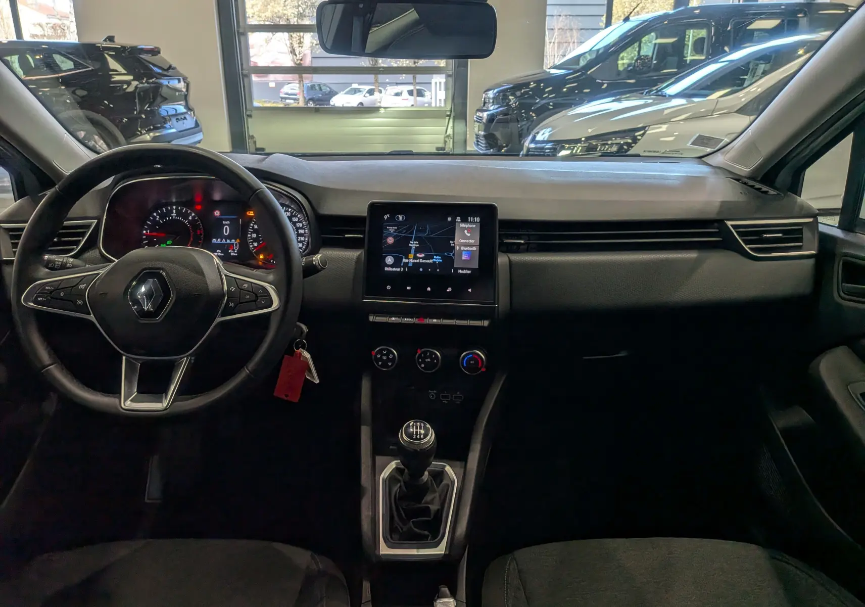 Vue intérieure avant de la Renault Clio V Business 2020, tableau de bord noir avec écran tactile et levier de vitesses manuel.
