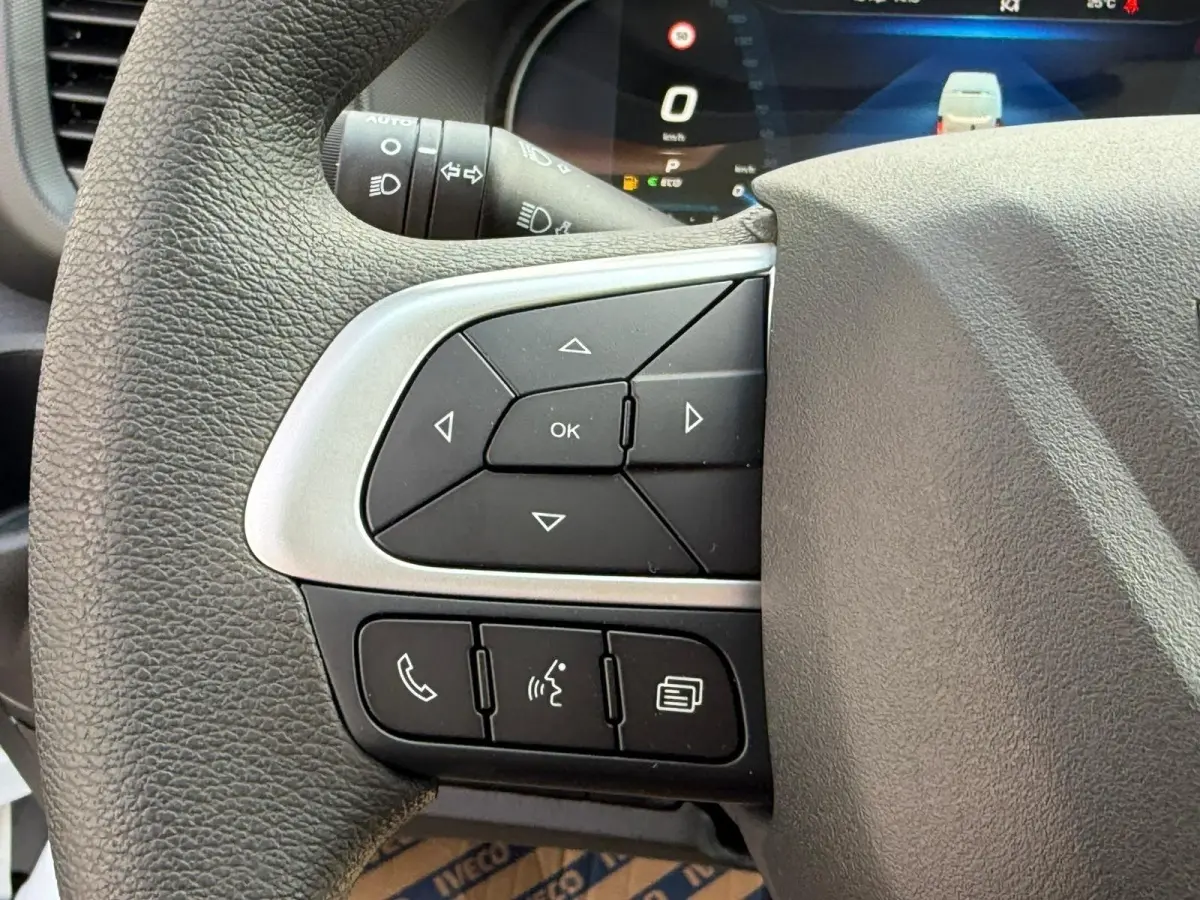 Gros plan sur les commandes au volant du côté gauche du Iveco Daily blanc 2026, avec écran numérique en arrière-plan.