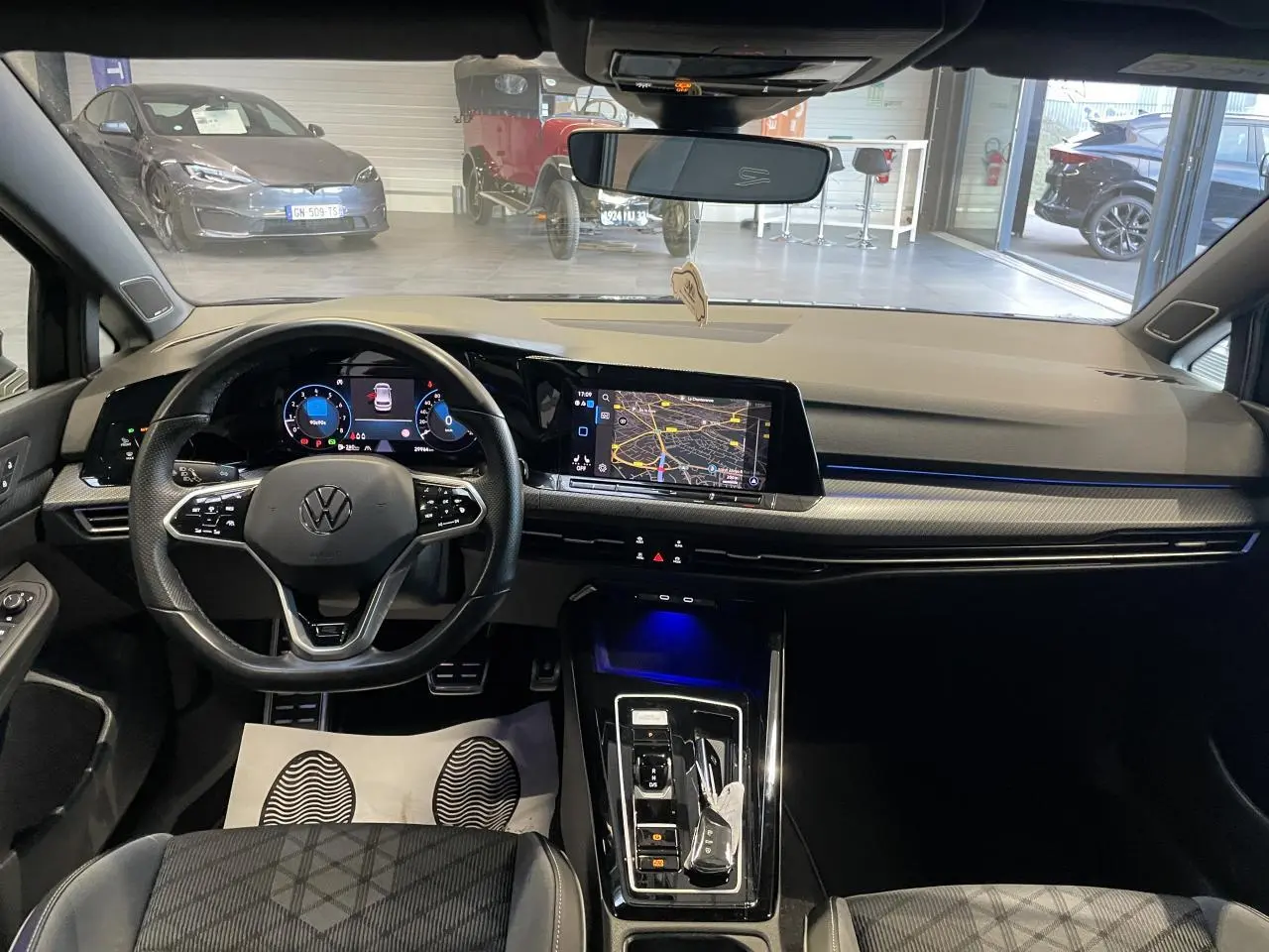 Vue intérieure avant de la Volkswagen Golf VIII R-Line noire, tableau de bord avec écran tactile et volant multifonctions cuir.