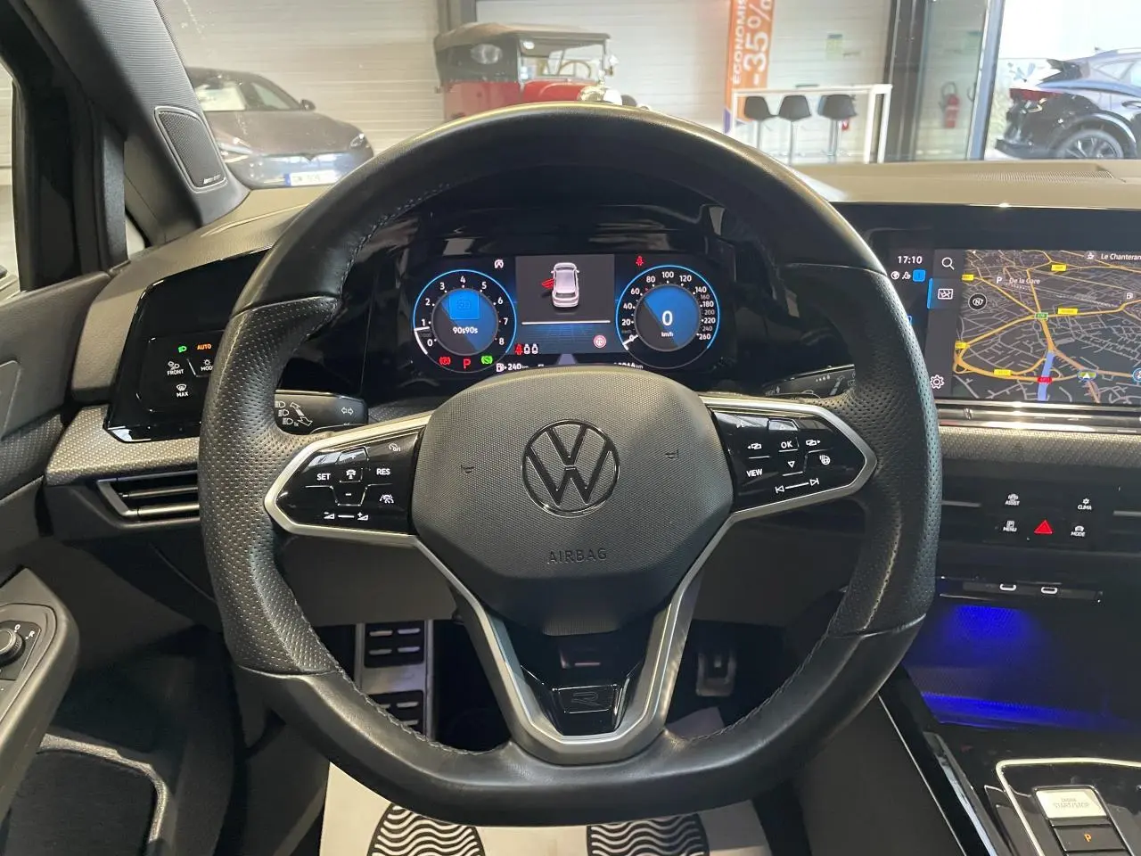 Vue intérieure centrée sur le volant cuir noir multifonctions de la Volkswagen Golf VIII R-Line avec tableau de bord digital et écran tactile.
