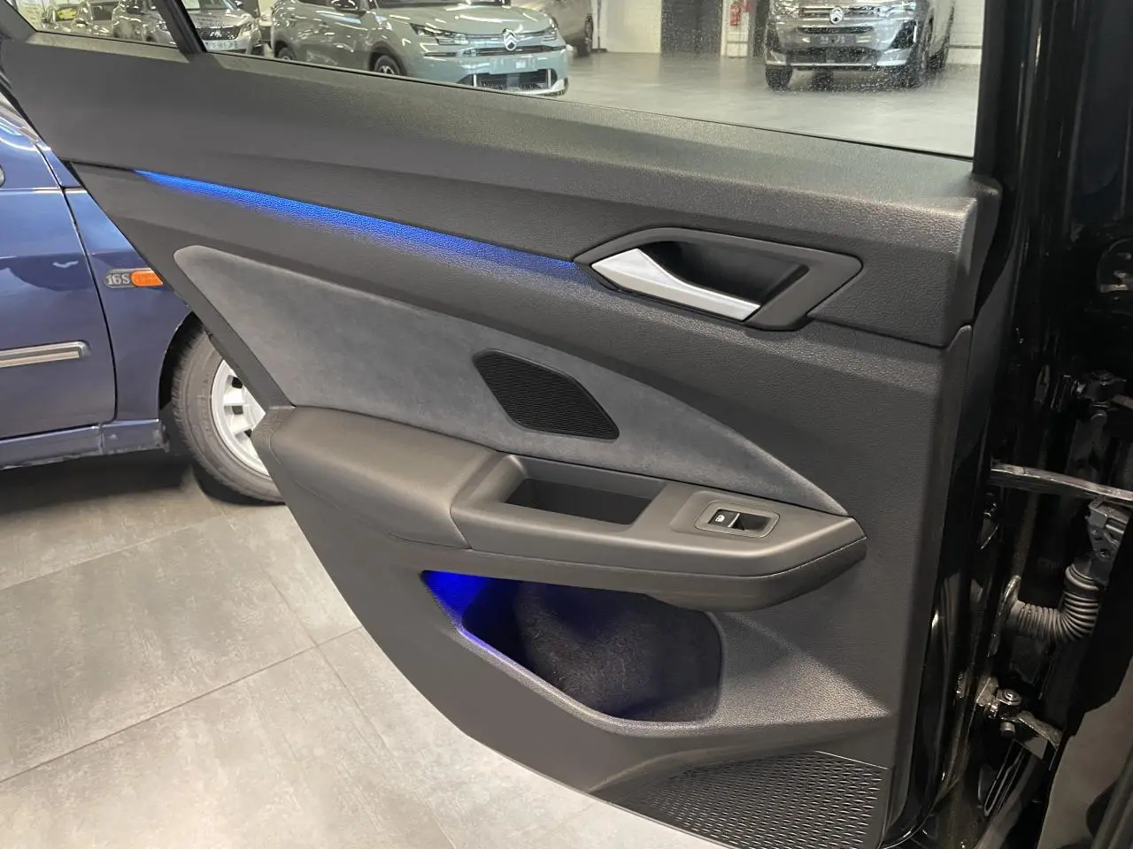 Vue intérieure de la porte arrière droite noire métallisée de la Volkswagen Golf 1.5 eTSI VIII R-Line avec éclairage d’ambiance bleu.