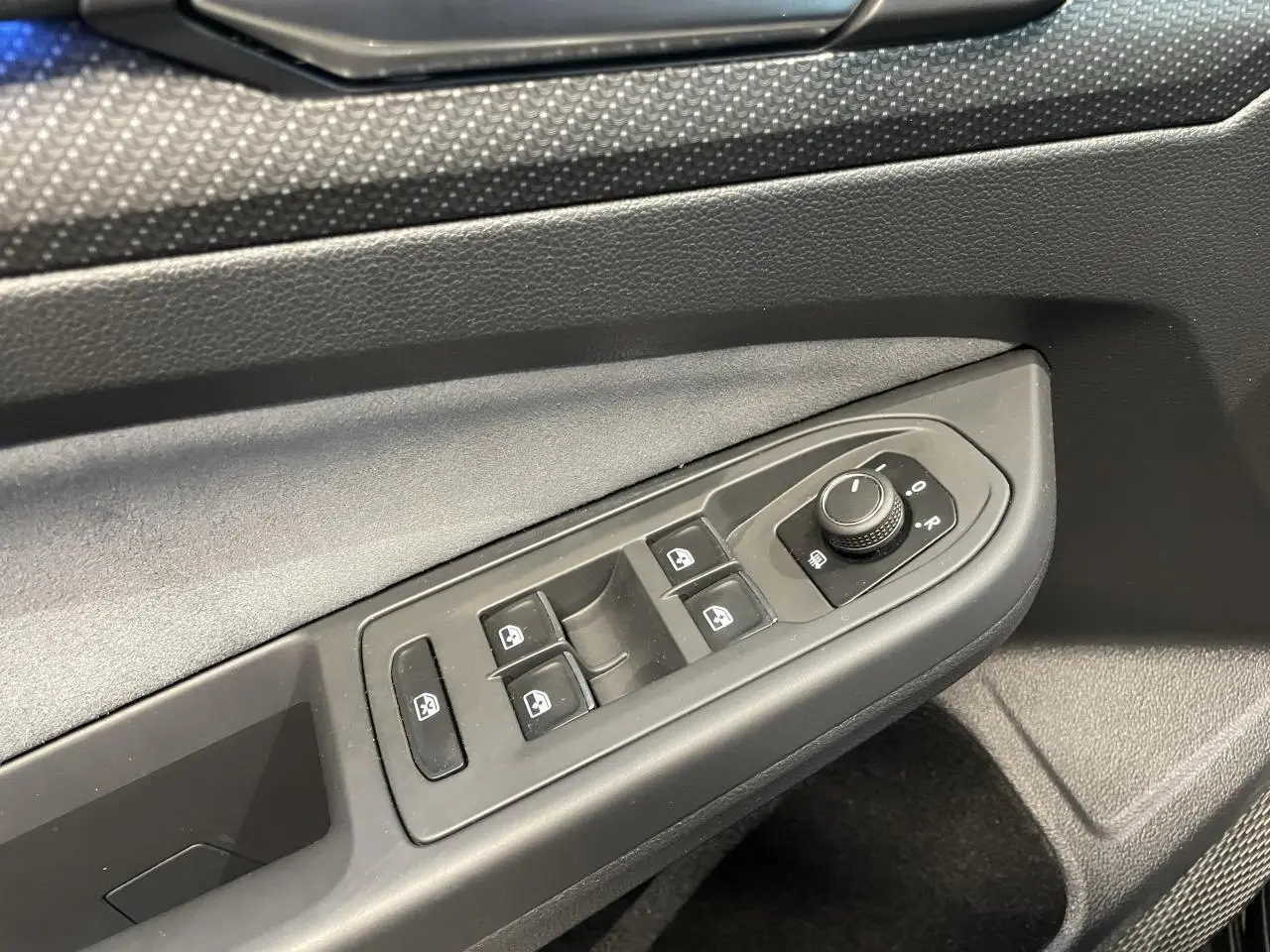 Détail des commandes de lève-vitres et réglage des rétroviseurs côté conducteur de la Volkswagen Golf VIII R-Line noire.