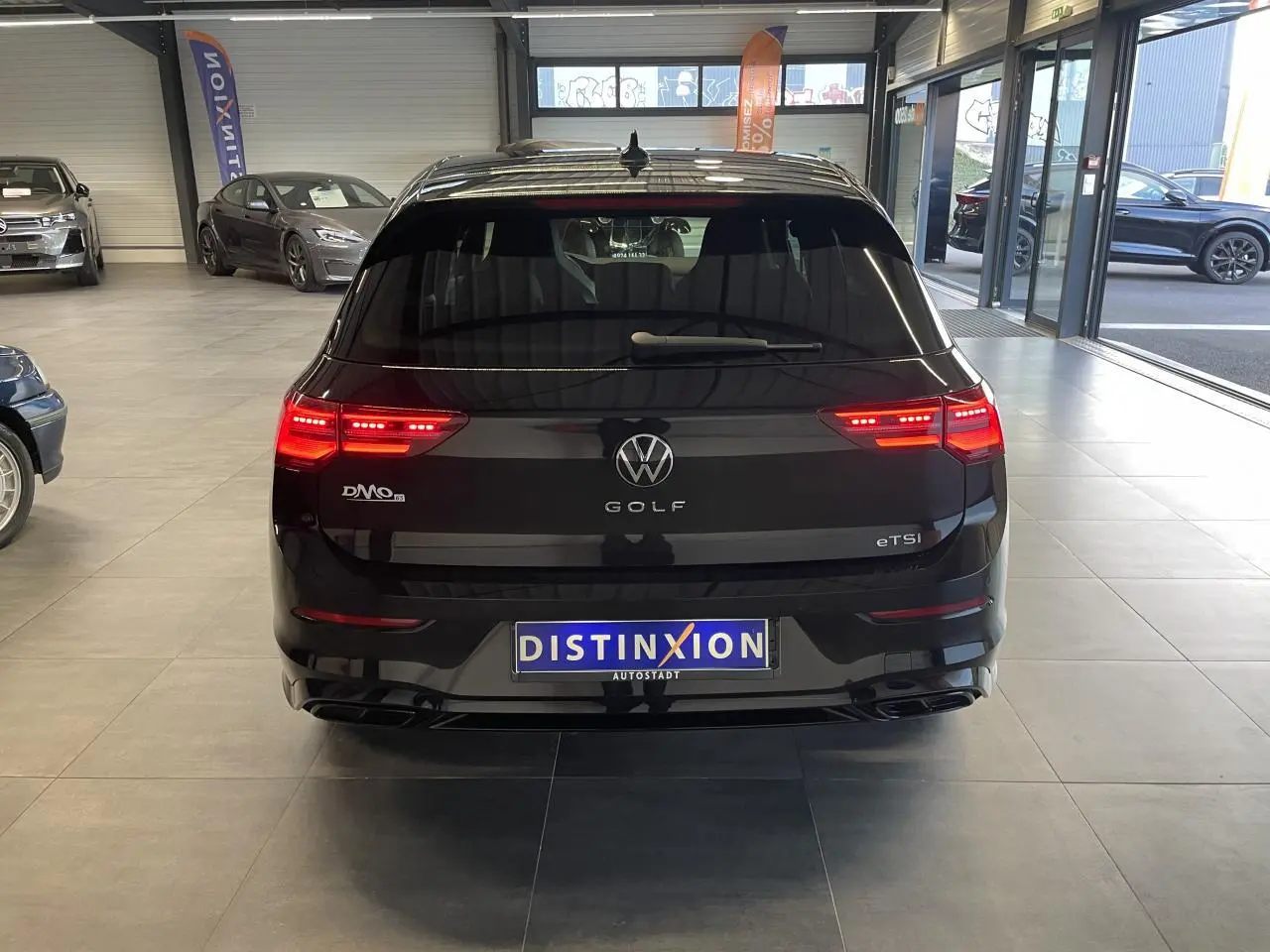 Vue arrière d'une Volkswagen Golf 1.5 eTSI noire métallisée avec feux LED allumés en showroom.