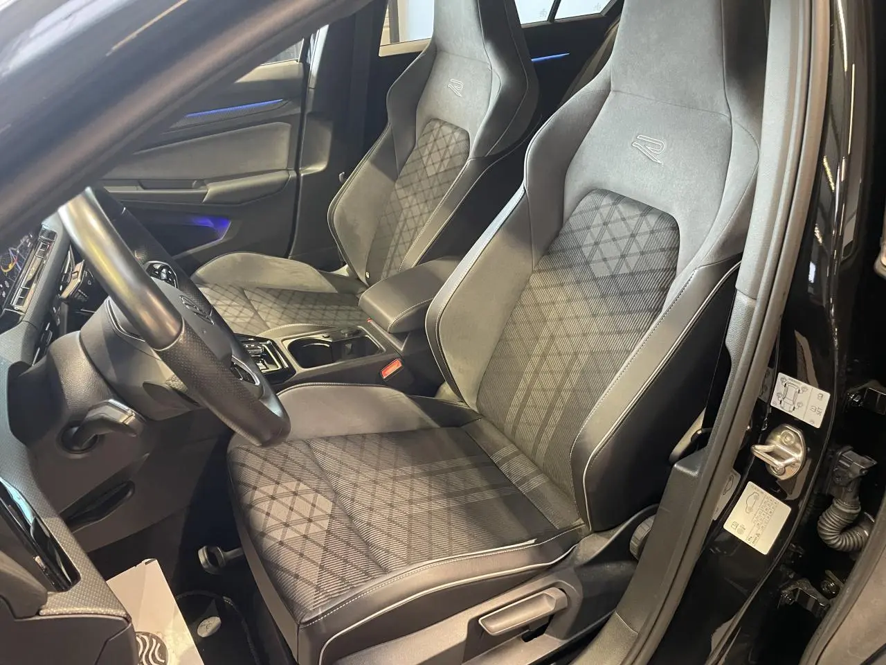 Vue intérieure côté conducteur de la Volkswagen Golf VIII R-Line Black 2024 avec sièges sport gris à motif losanges.