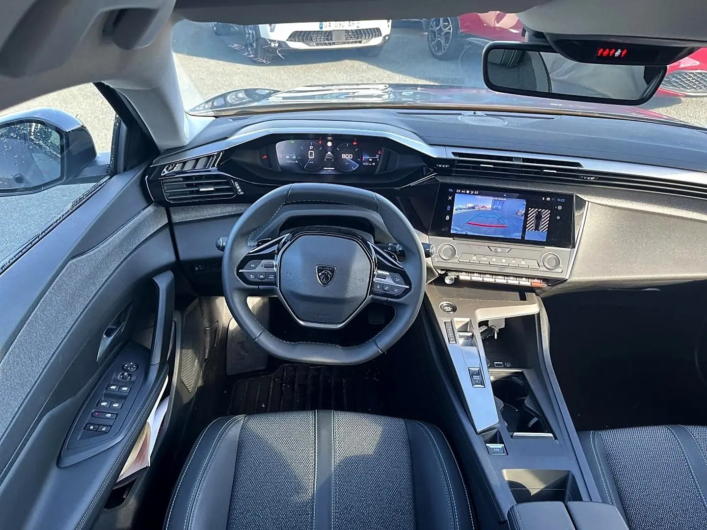 Intérieur de la Peugeot 308 2025 vue de face, tableau de bord noir avec écran tactile et volant compact multifonction.