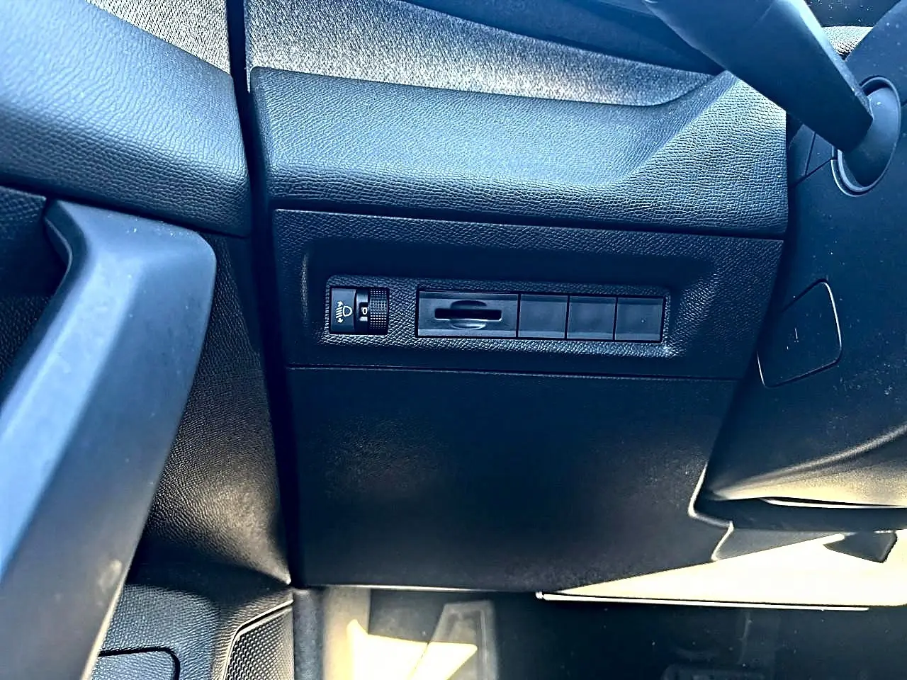 Détail intérieur côté gauche montrant les commandes d'éclairage et la texture noire du tableau de bord du Peugeot 308 gris selenium.