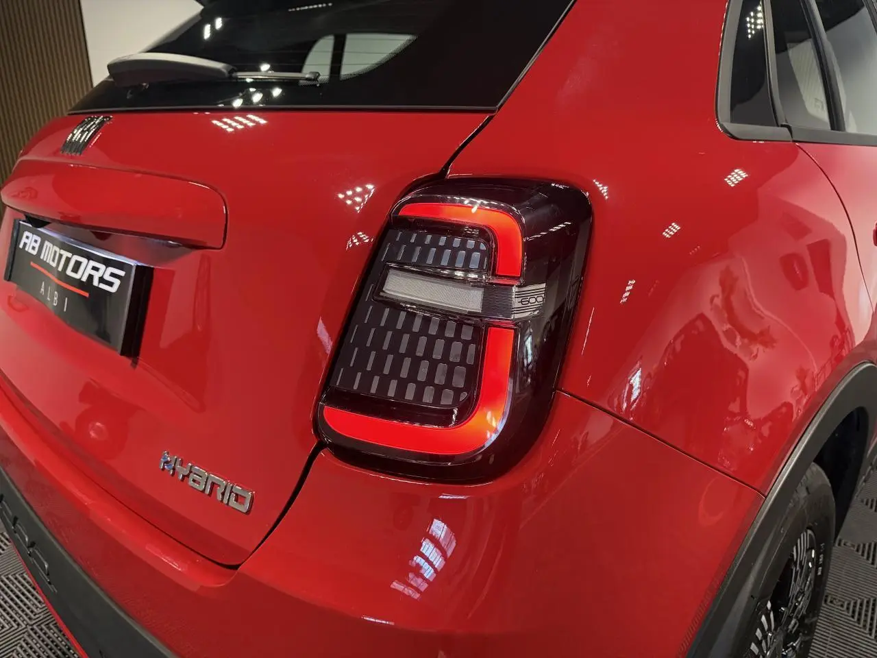 Vue 3/4 arrière droite d'une FIAT 600 rouge foncé avec feux arrière LED en forme de U et logo Hybrid sur le hayon.