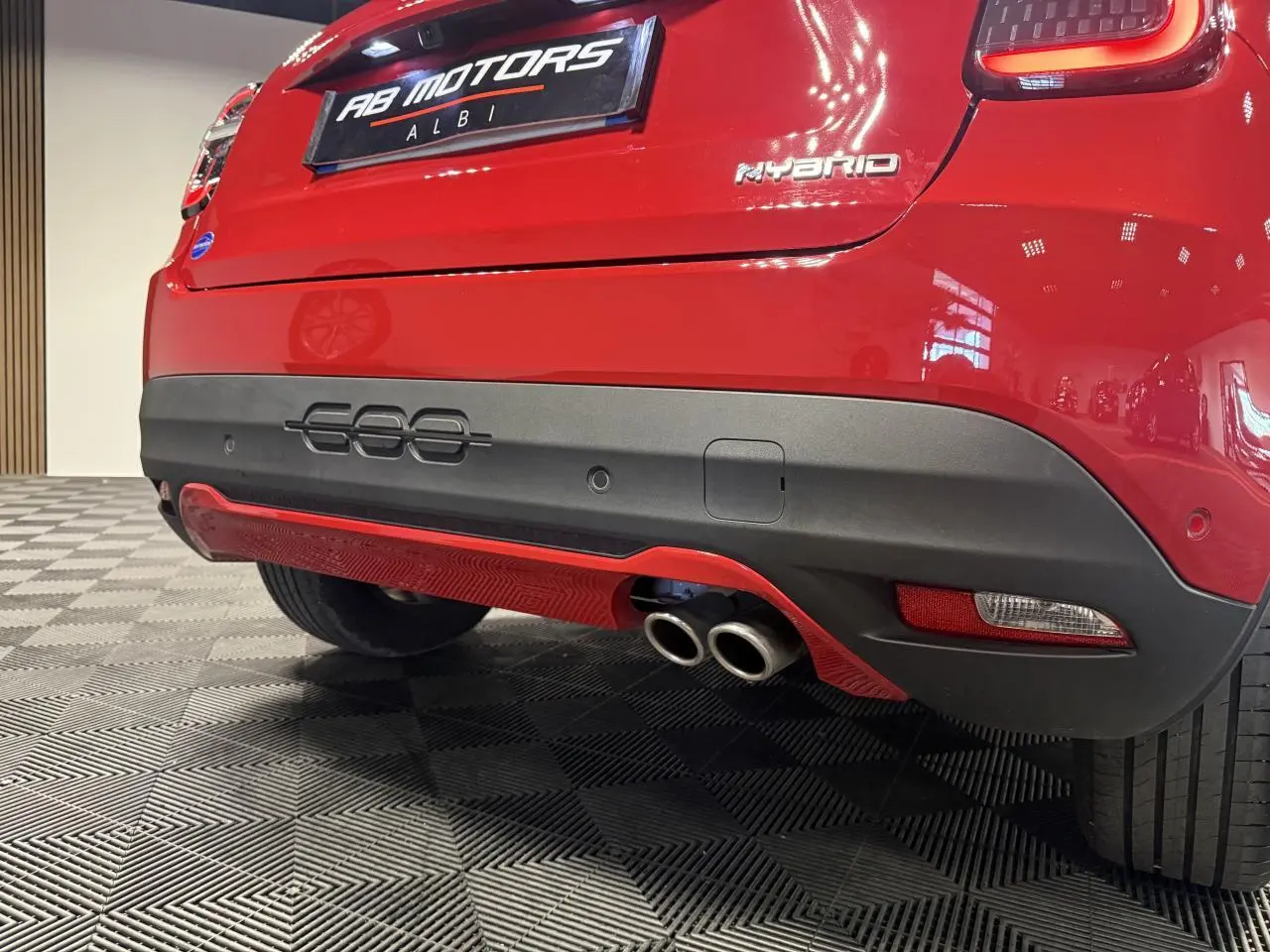 Vue 3/4 arrière droite de la FIAT 600 rouge foncé avec double sortie d’échappement et logo Hybrid sur hayon.