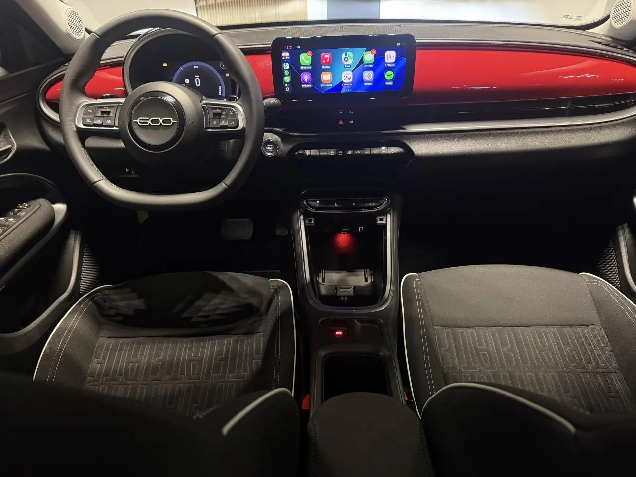 Vue intérieure avant de la Fiat 600 2025, tableau de bord rouge foncé avec écran tactile et volant noir marqué 600.