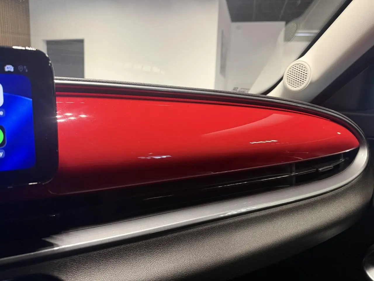 Détail intérieur du tableau de bord rouge foncé de la FIAT 600 Hybrid 2025 avec écran tactile partiel visible à gauche.