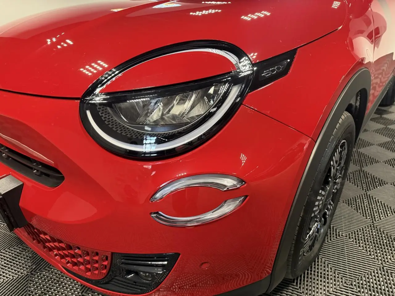 Gros plan sur l'avant droit rouge foncé du FIAT 600 Hybrid 2025, mettant en valeur le phare LED et la calandre distinctive.