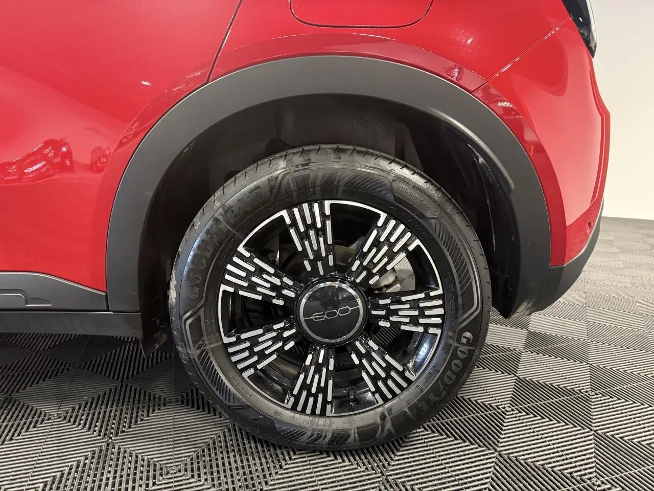 Gros plan sur la roue arrière droite d'une FIAT 600 rouge foncé avec jante noire et détails blancs stylisés.