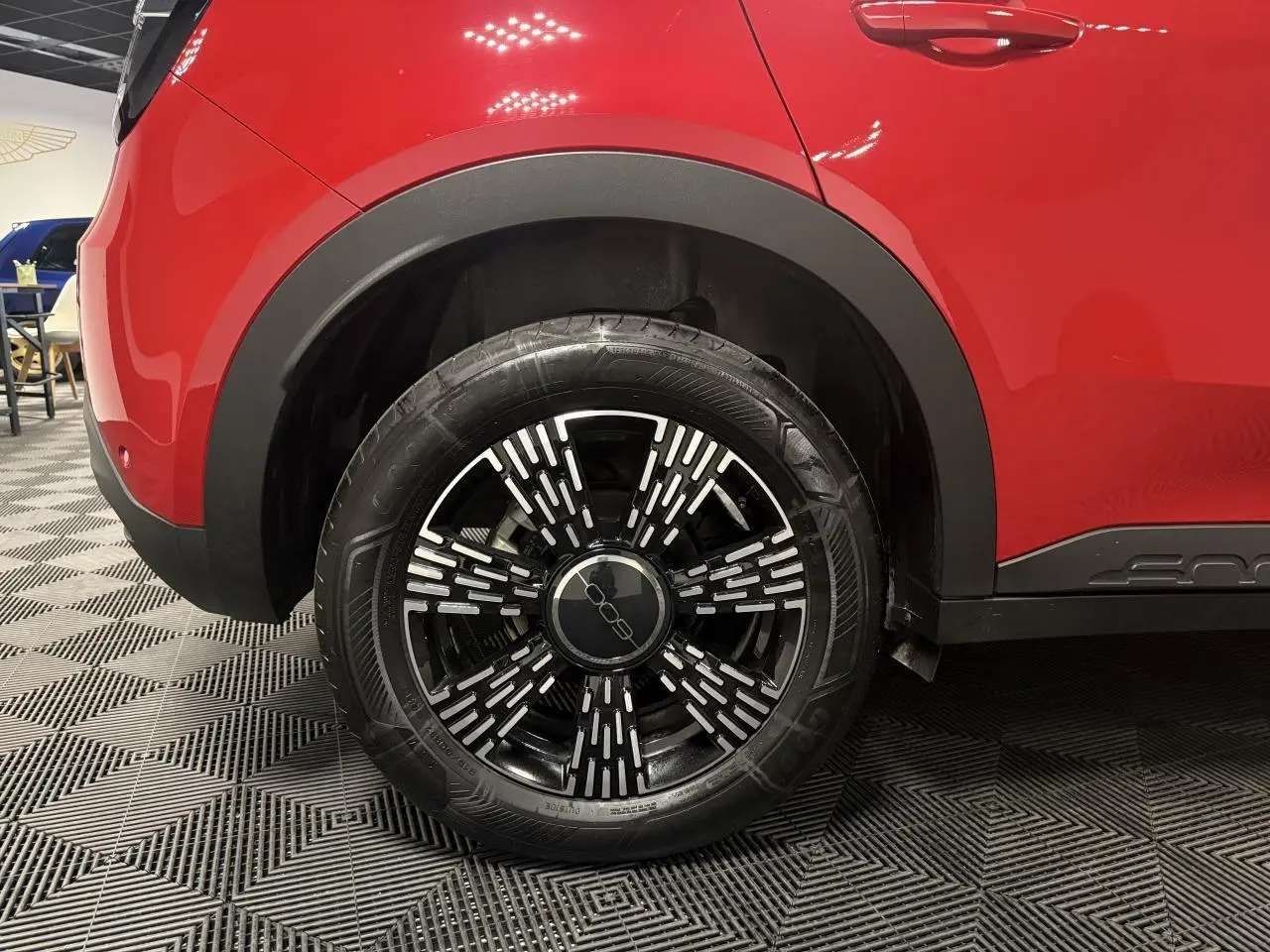 Gros plan sur la roue arrière droite d'une FIAT 600 rouge foncé avec jante noire et détails argentés.