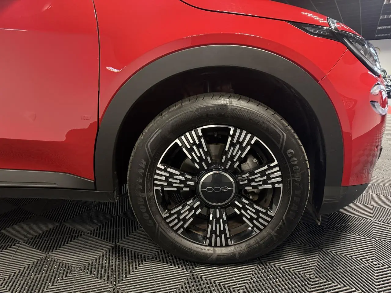 Gros plan sur la roue avant droite d'une FIAT 600 rouge foncé avec jante noire et motifs argentés.