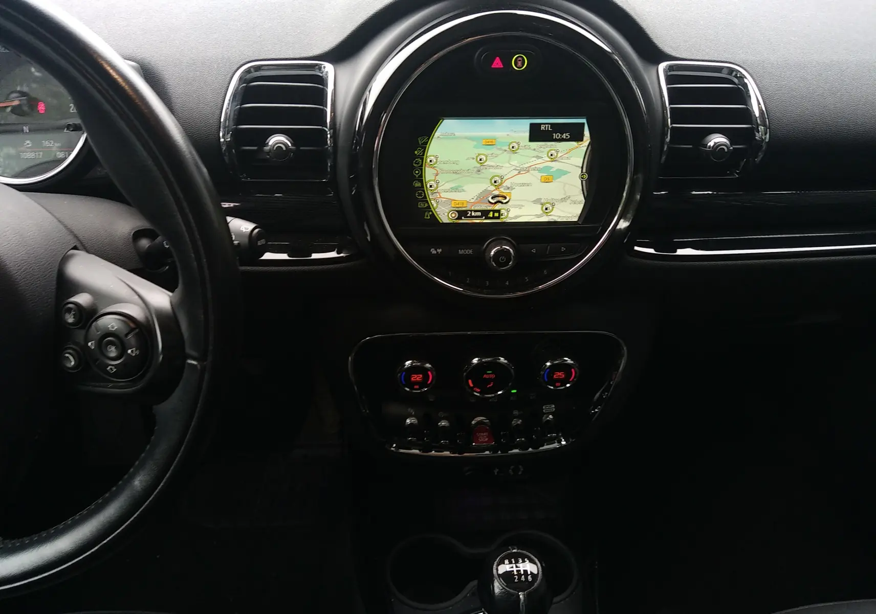 Vue intérieure centrée sur le tableau de bord noir du MINI CLUBMAN F54 avec écran GPS rond et levier de vitesse manuel.