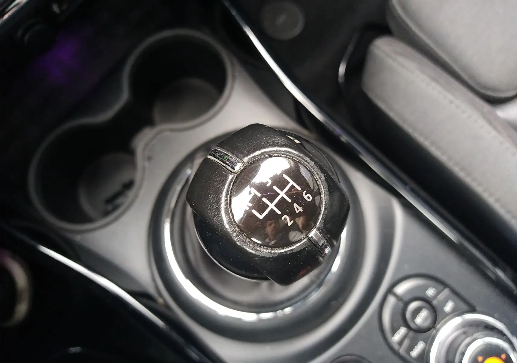 Gros plan sur le levier de vitesse manuel noir de la MINI CLUBMAN F54, entouré de la console centrale et porte-gobelets.