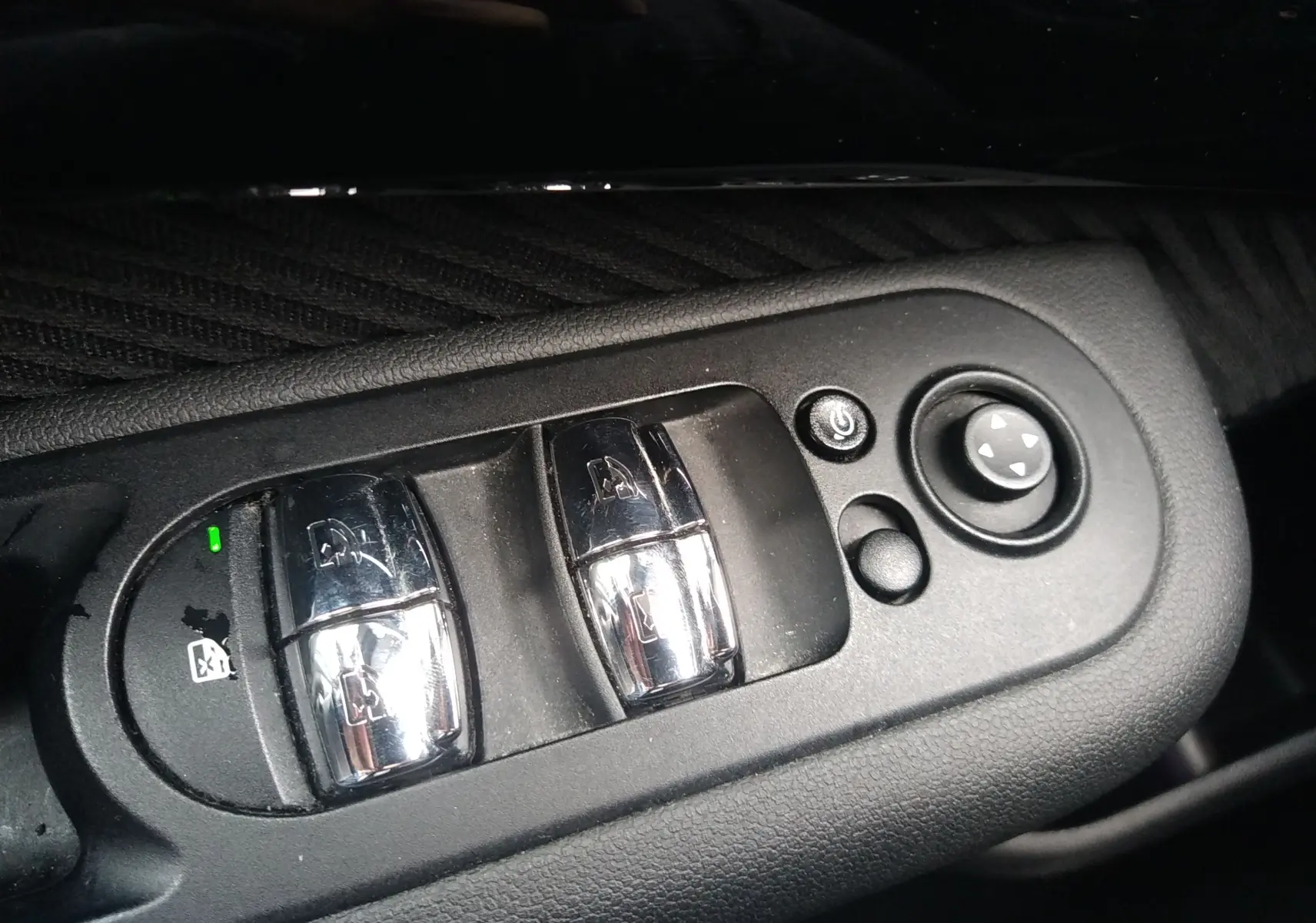 Gros plan sur les commandes de lève-vitres et réglage des rétroviseurs côté conducteur d'une MINI Clubman F54 argentée.