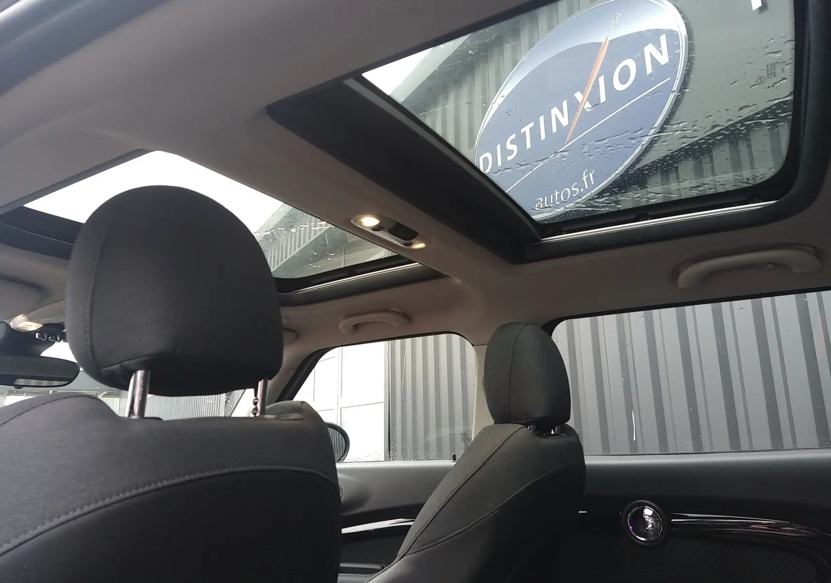 Vue intérieure arrière de la MINI CLUBMAN F54 Silver Metal, mettant en valeur le toit panoramique et les sièges noirs.