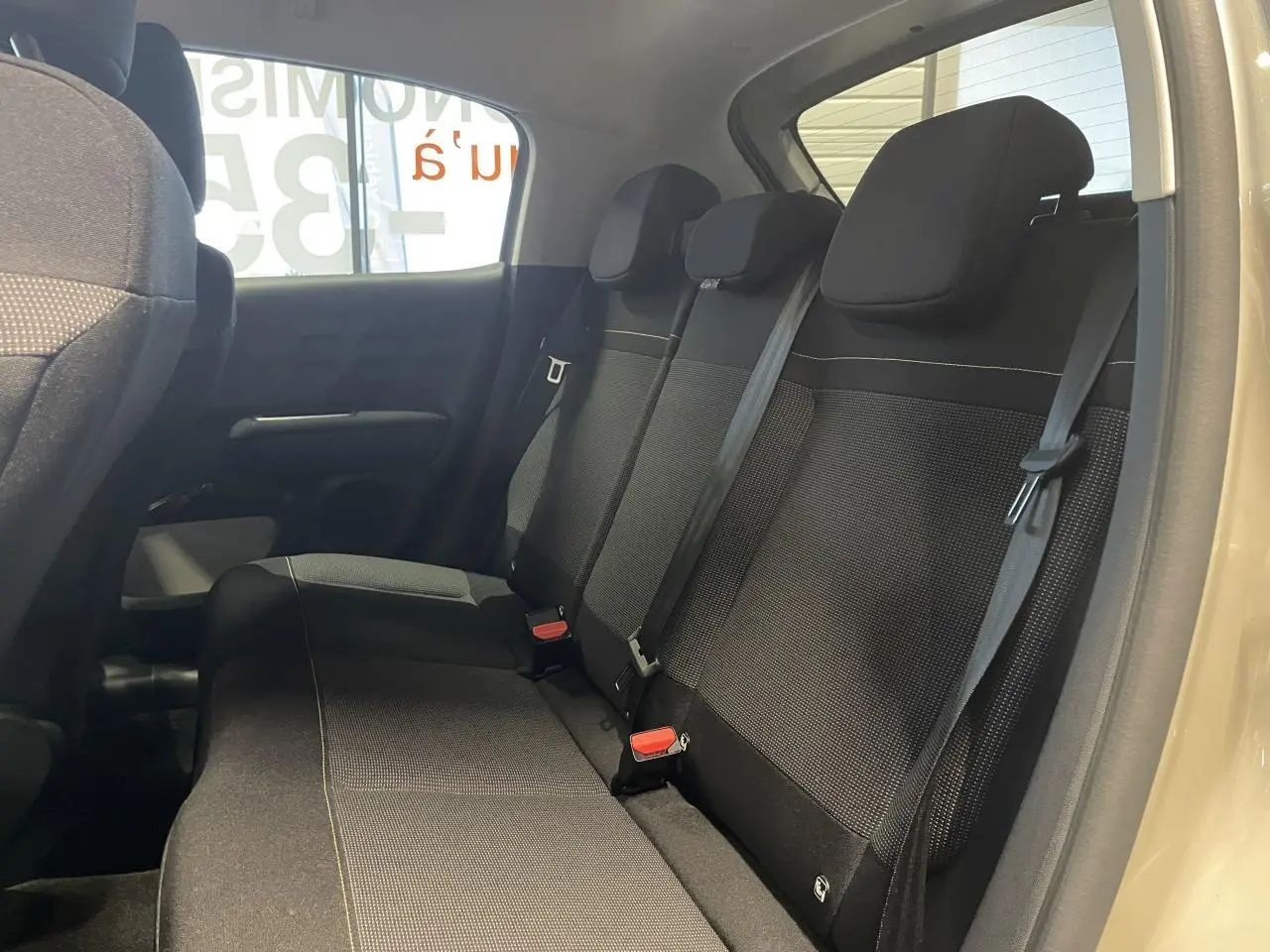 Vue intérieure côté droit de la banquette arrière noire de la Citroën C3 beige clair 2024 avec ceintures visibles.