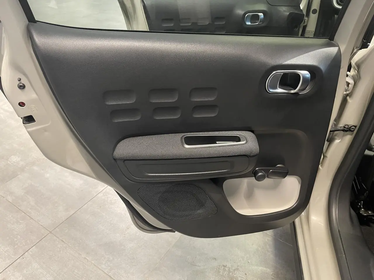 Vue rapprochée de la porte arrière gauche beige clair d'une Citroën C3 2024 avec poignée chromée et manivelle de vitre.