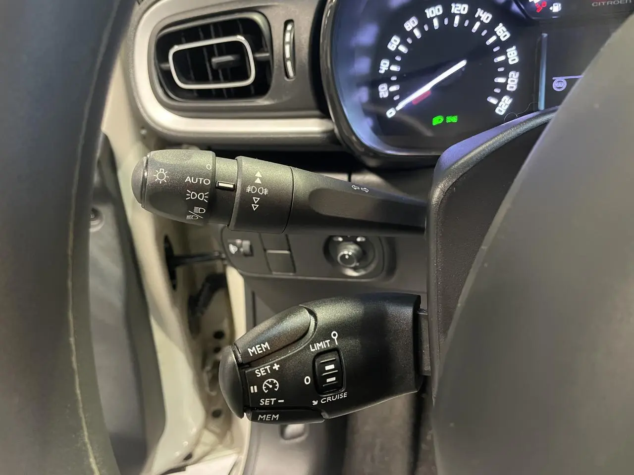 Gros plan sur les commandes au volant gauche de la Citroën C3 beige clair 2024, avec tableau de bord éclairé.