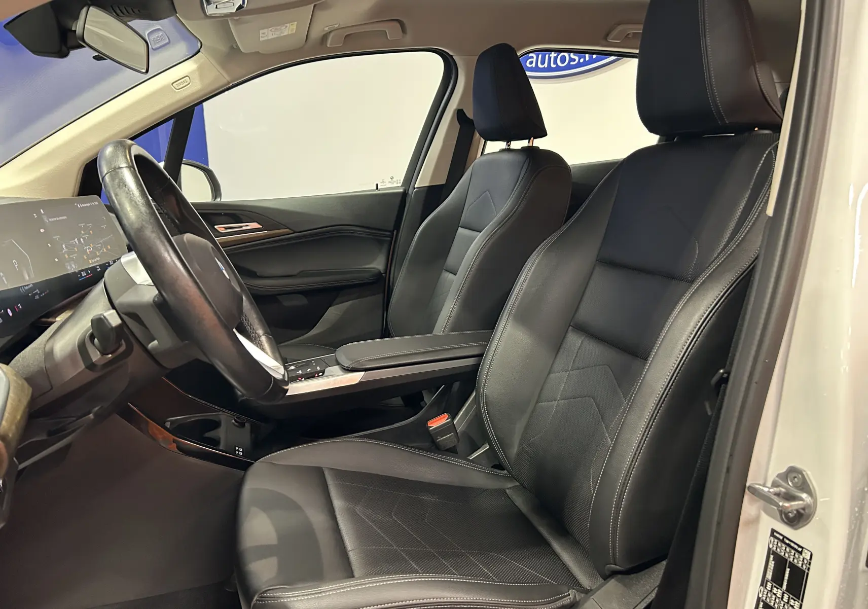 Vue intérieure côté conducteur de la BMW Série 2 Active Tourer blanche, sièges cuir noir et tableau de bord moderne.