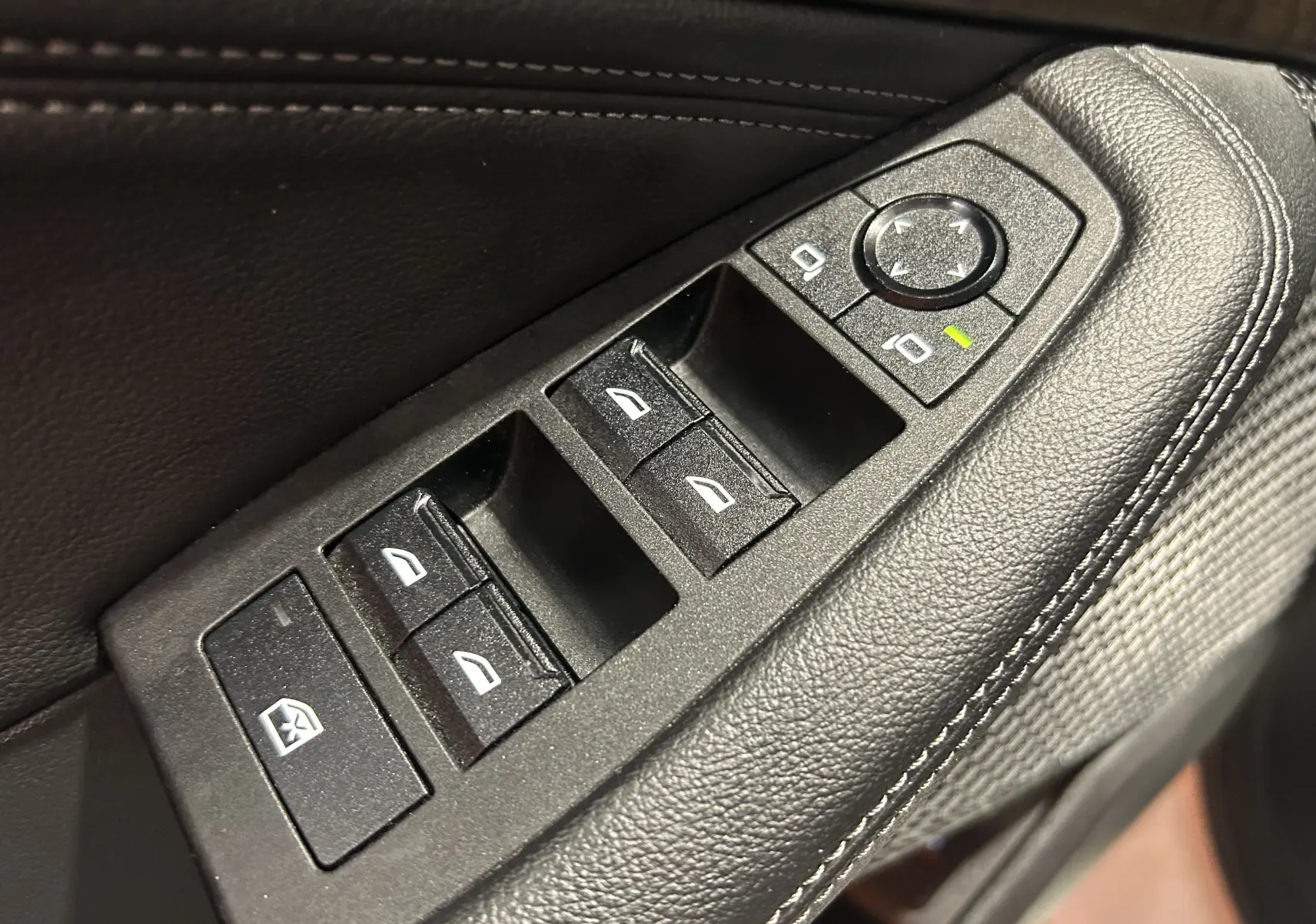 Gros plan sur les commandes de lève-vitres et réglage des rétroviseurs côté conducteur en cuir noir sur BMW Série 2 Active Tourer.