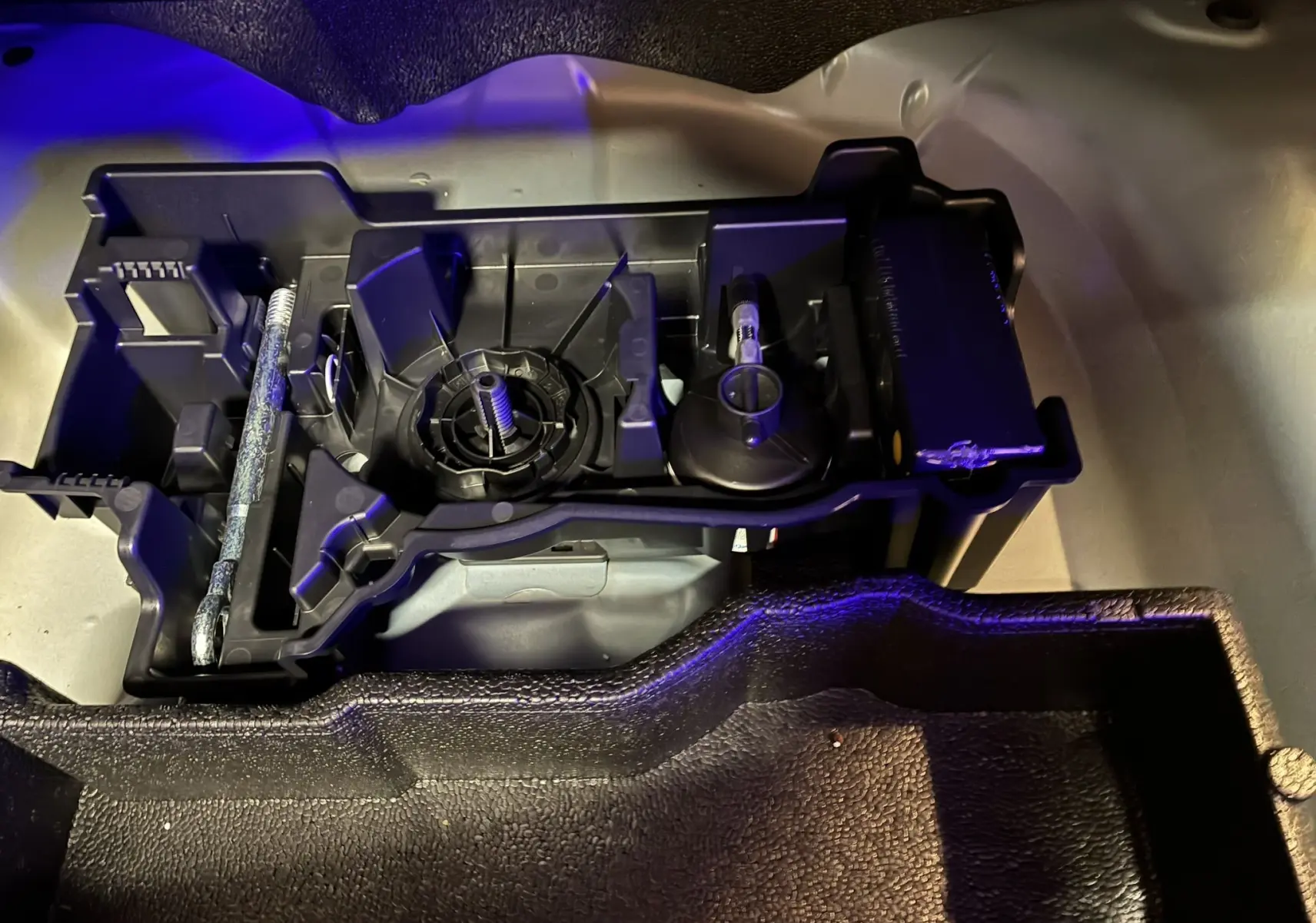 Vue rapprochée du rangement d'outils sous le plancher du coffre d'un Peugeot 2008 bleu 2025, avec support plastique noir.
