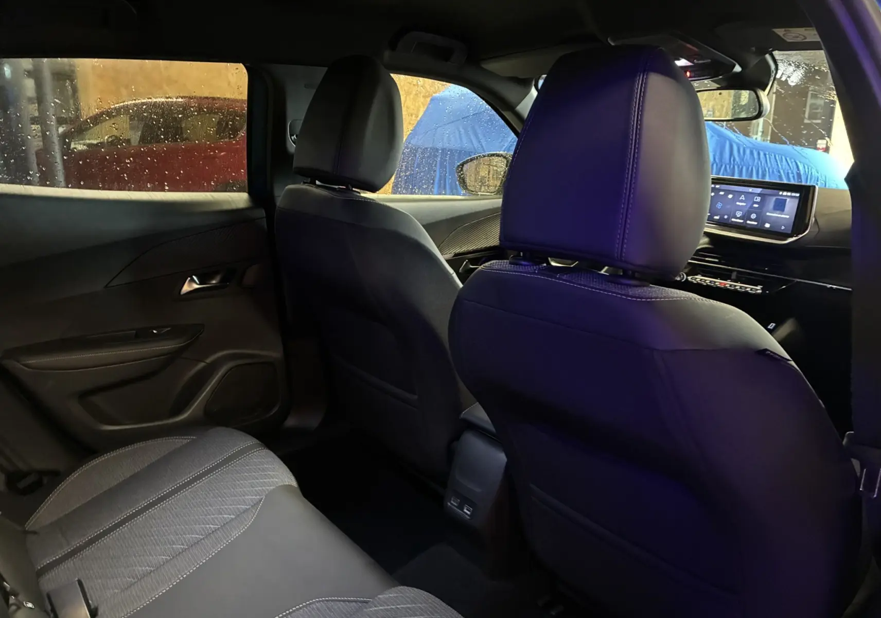 Vue intérieure arrière droite du Peugeot 2008 bleu 2025, montrant les sièges en tissu noir et l'écran tactile du tableau de bord.