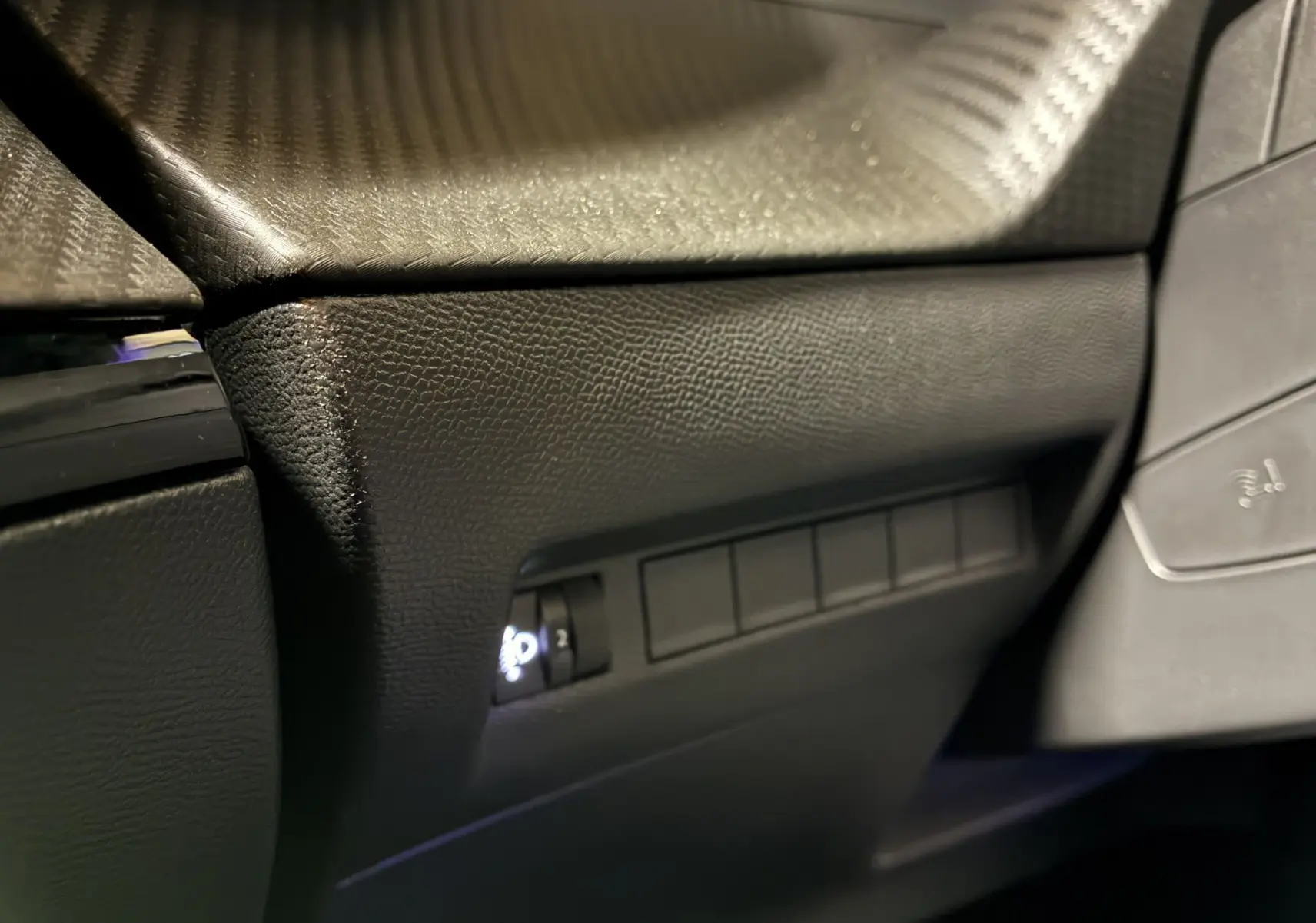 Gros plan sur la partie inférieure gauche du tableau de bord noir texturé du Peugeot 2008 1.2 Hybrid 136 Allure.