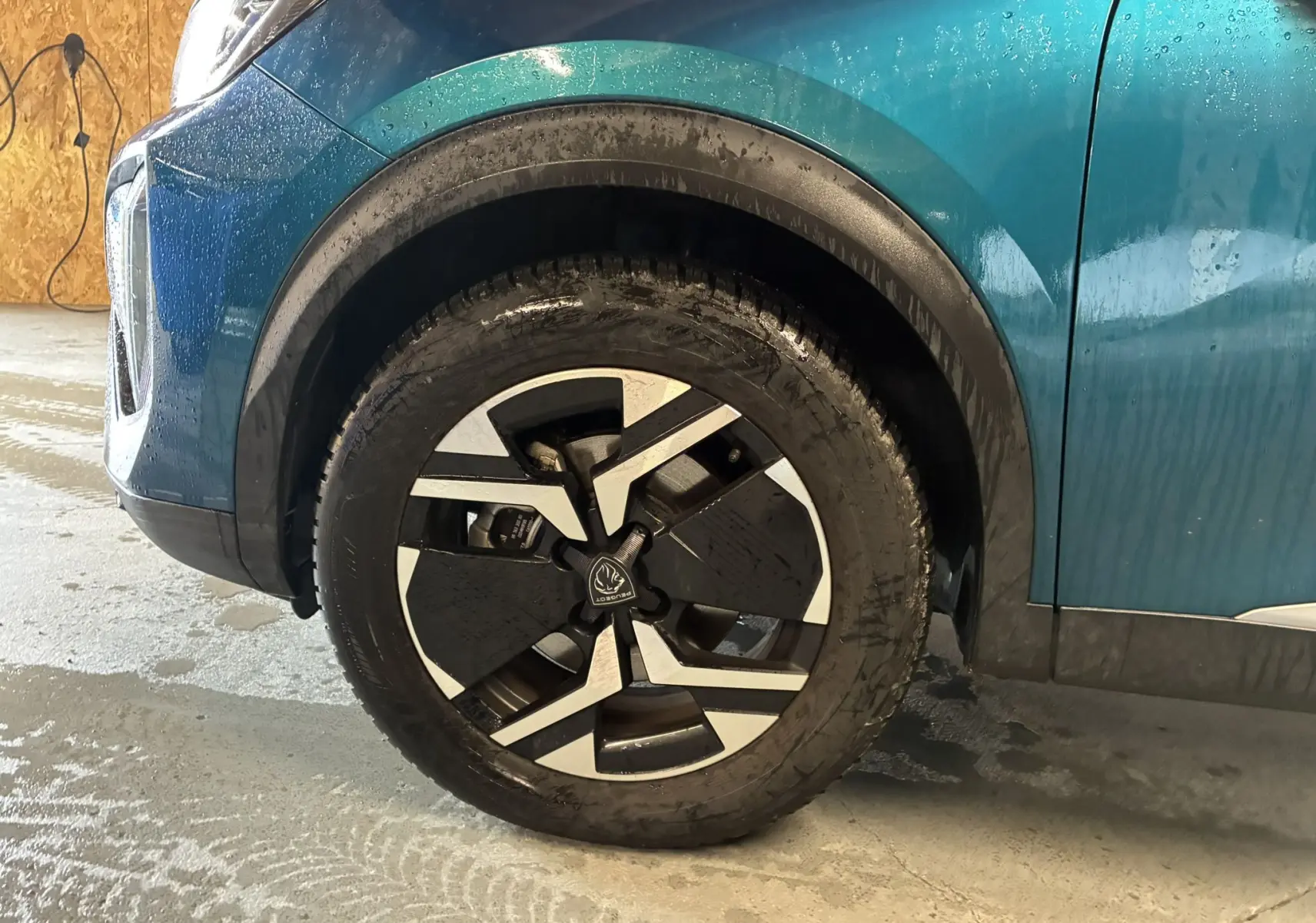 Gros plan sur la roue avant gauche d’un Peugeot 2008 bleu 2025, avec jante au design noir et argent moderne.