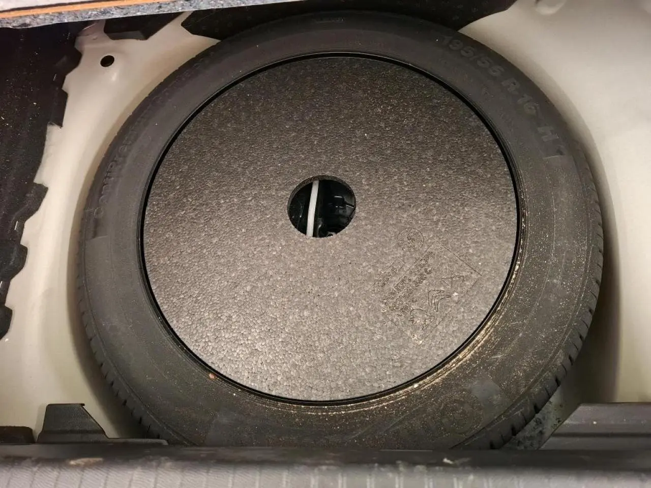 Vue rapprochée du pneu de secours noir logé dans le coffre d'une Peugeot 208 blanche de 2020.