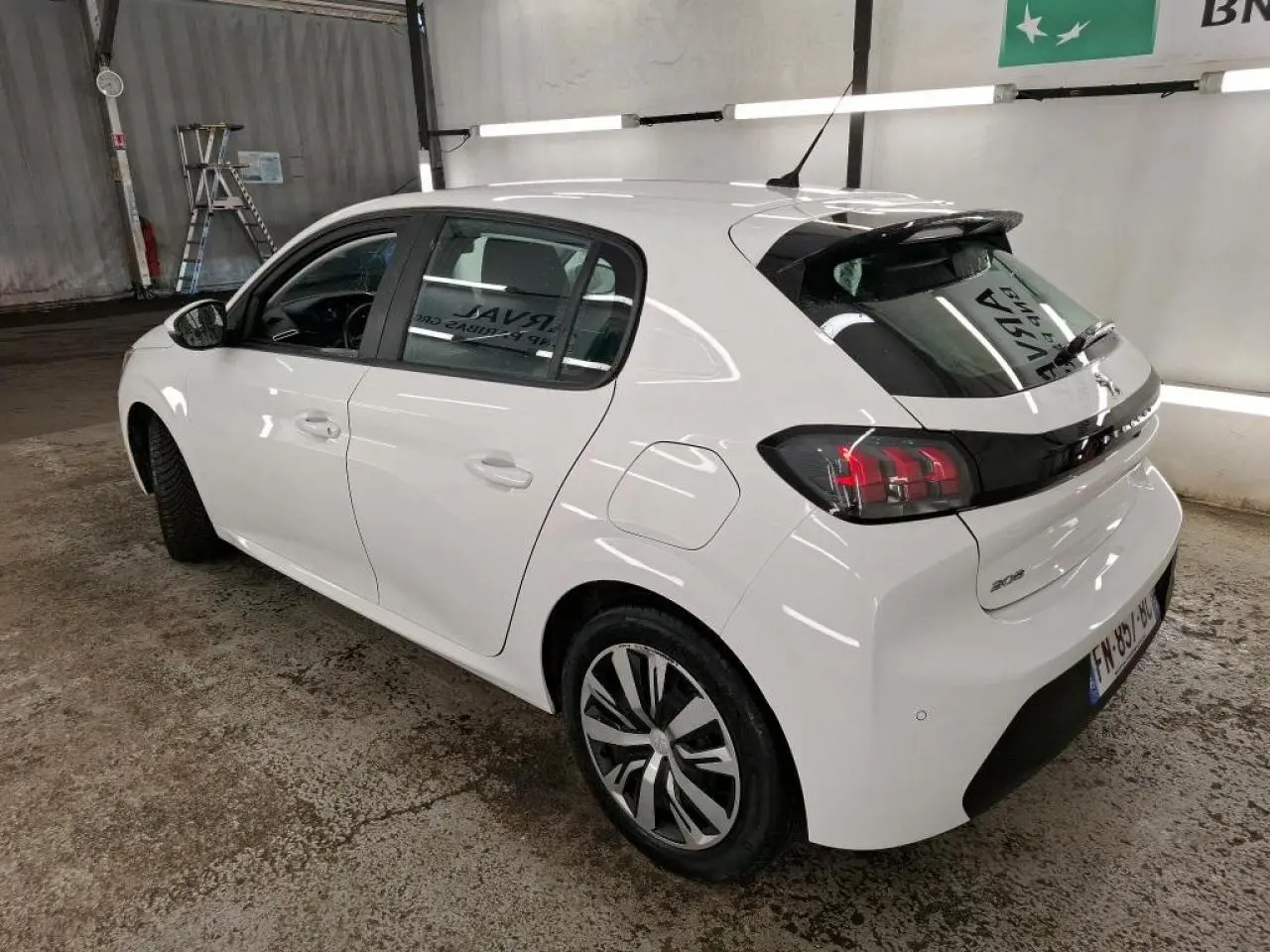Peugeot 208 blanche vue 3/4 arrière droit en intérieur, avec jantes alliage et feux arrière distinctifs noirs.