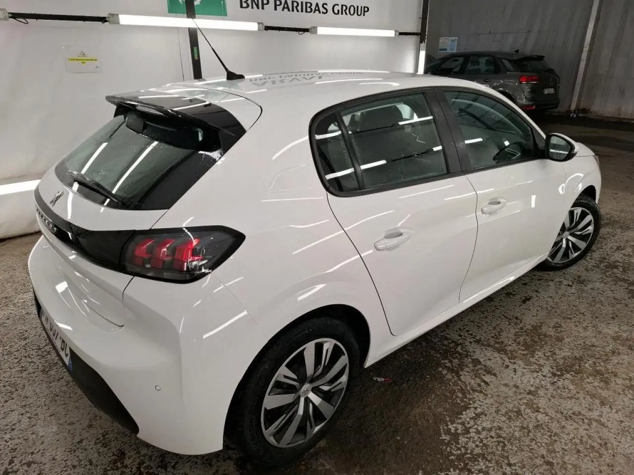 Peugeot 208 blanche vue 3/4 arrière droit, avec feux arrière noirs et jantes alliage bicolores.
