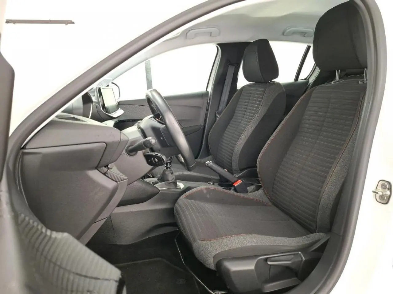 Vue intérieure côté conducteur de la Peugeot 208 blanche, montrant les sièges tissu gris et le volant compact noir.