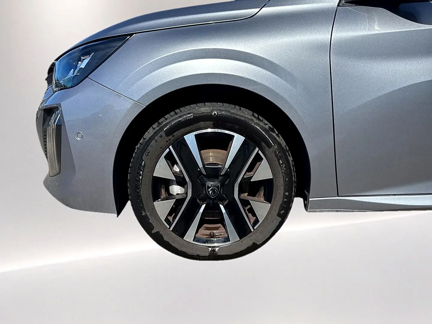 Gros plan sur la roue avant gauche et l'aile d'une Peugeot 208 gris artense avec jante alu au design moderne.
