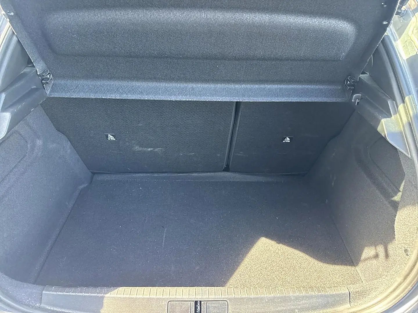 Coffre ouvert en vue plongeante d'une Peugeot 208 gris artense, montrant l'espace de chargement et la banquette arrière rabattable.