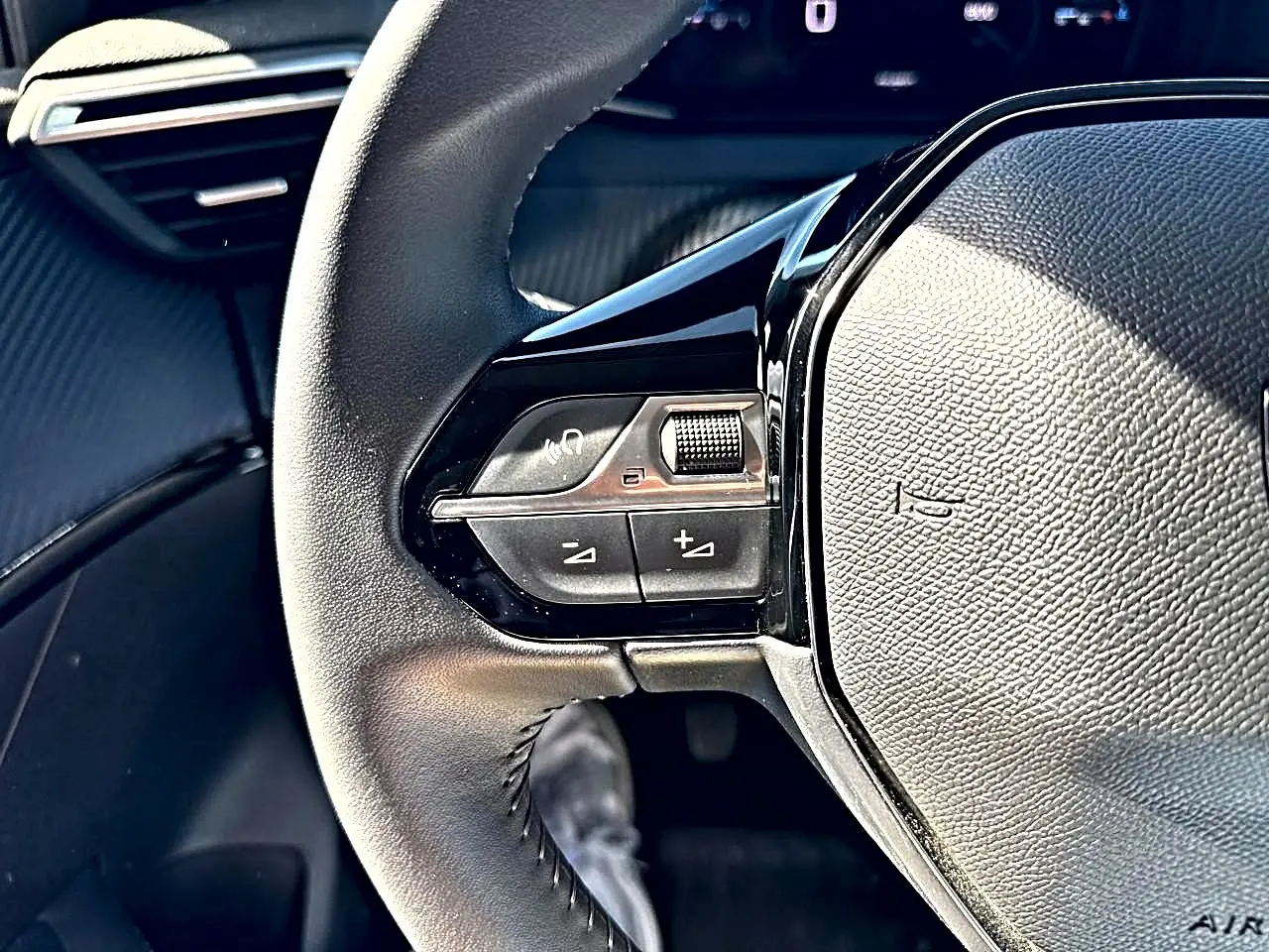 Gros plan sur les commandes au volant à gauche de la Peugeot 208 1.2 100 Allure, intérieur noir texturé.
